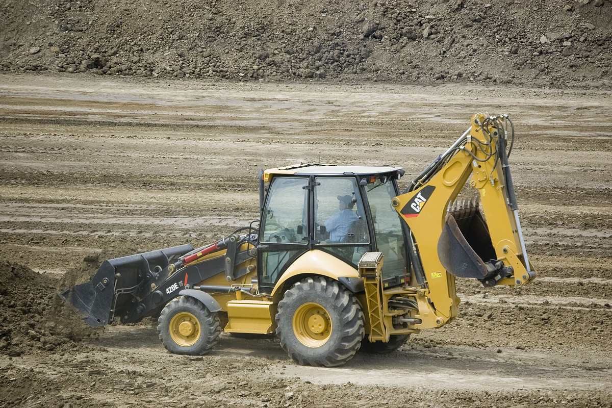 Retroexcavadora amarilla trabajando sobre un terreno de tierra